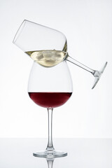 Two wineglasses on top of one another with red and white wine with ice cubes served on table with reflection against white background prepared for party celebration