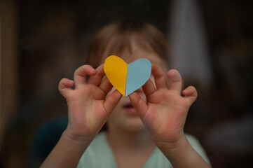 Little toddler child holding a heart shaped paper in the colors of ukrainian flag