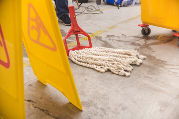 A janitor cleans the surface of a wet concrete floor of a factory with a string mop. A wet floor...