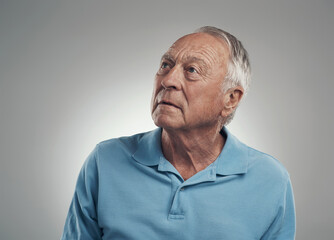 I think I see something over there. Shot of an older man looking off into the distance in a studio against a grey background.