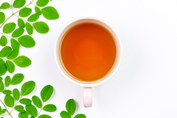 Moringa Tea in ceramic cup with fresh green leaf isolated on white background, top view. Moringa oleifera tropical herb healthy lifestyle concept.