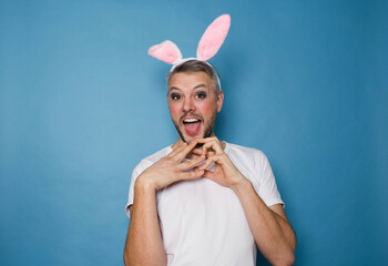 An LGBT gay man smiles on a blue background with rabbit ears on his head