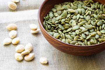 Raw peeled pumpkin seeds in a clay plate on a canvas tablecloth