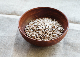 Raw peeled sunflower seeds in a clay plate on a canvas tablecloth