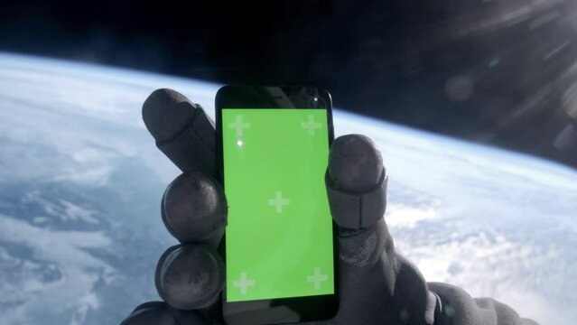 View through the helmet, astronaut using his mobile phone during the spacewalk. Green screen chroma key. Earth in the background