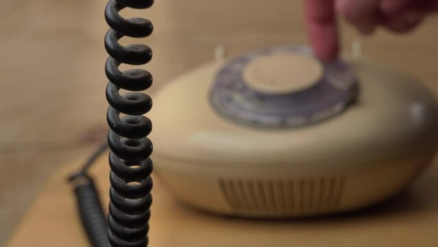 Dialing a number on an old vintage wire telephone, pick up the phone and call. Vintage stationary beige communication device. Vintage telephone dialing.
