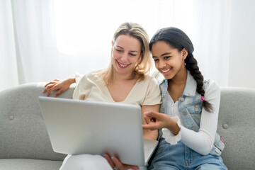 Adorable black teen daughter with mother sit on sofa at home with laptop