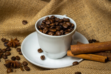 Coffee cup full of coffee beans. Roasted coffee beans on burlap.
