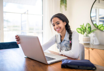 African American teen girl learning school tasks at home, writing notes and using laptop on the kitchen table