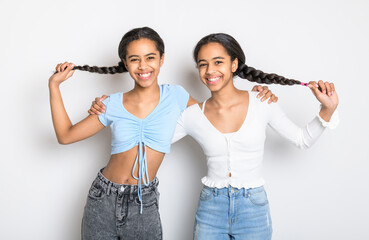 Adorable black twin teen girl on studio white background holding her braided