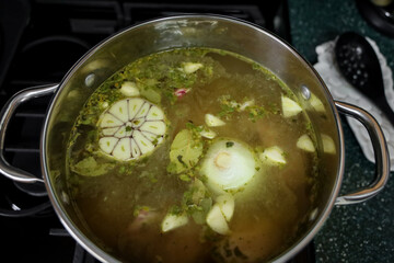View of a pot with chicken, water, garlic head and onion cut in half, bay leaves and spices for making pozole.