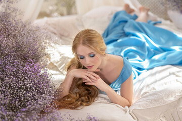 Tender blond girl in a sun-drenched bedroom on the bed