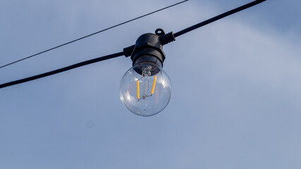 Decoration bulb on the wire outside with blue sky. Bulb outside on black wire