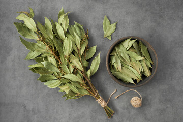 Bowl of dried laurel leaves and bunch of dry green bay leaves, top view, flat lay.