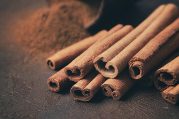 Aromatic cinnamon sticks and pile of sprinkled ground cinnamon on background. Selective focus.