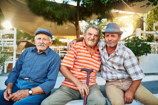 The Have Been Friends Since They Were Kids. Portrait Of A Group Of Cheerful Senior Men Sitting Together While Looking Into The Camera Outside.