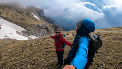 Fototapeta na wymiar Happy backpack couple on scenic hiking trail with view on cloud covered mountain peaks of the Hochschwab Region in Upper Styria, Austria. Dry alpine meadows in beautiful Alps, Europe. Freedom vibe