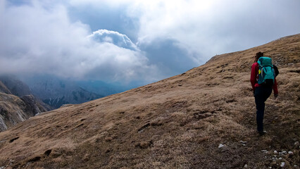 Woman with backpack on scenic hiking trail with view on cloud covered mountain peaks of the Hochschwab Region in Upper Styria, Austria. Dry alpine meadows in beautiful Alps, Europe. Freedom vibe. Rain