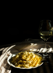 Pasta with cheese and black ground pepper. A glass of white wine