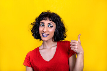 Smiling young woman in red t-shirt is showing thumb. Woman portrait with trendy look and bright colors on yellow background.