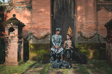 Balinese teens girl and boy together posing in traditional bali costume in old Hindu temple.