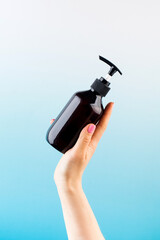 Mockup of a brown dispenser with a natural cosmetic product in a female hand on a blue background.