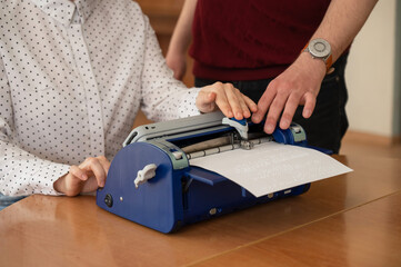 A man teaches a blind woman to type on braille machine. 