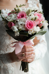 Portrait of the bride. Attractive young girl look at the camera in a white wedding dress and veil holding a bouquet of white and pink flowers in her hands on a background of green trees