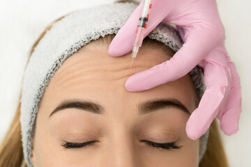 Close-up of the hands of an expert cosmetologist injecting botox into a woman's forehead. Correction of forehead and eye wrinkles with botulinum toxin - obrazy, fototapety, plakaty