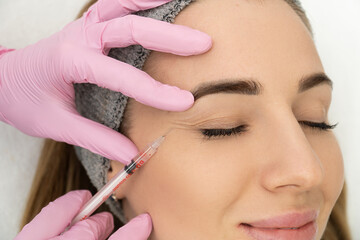 Close-up of the hands of an expert cosmetologist injecting botox into a woman's forehead....