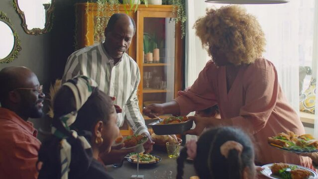 Hospitable African American woman serving food for guests at family home dinner