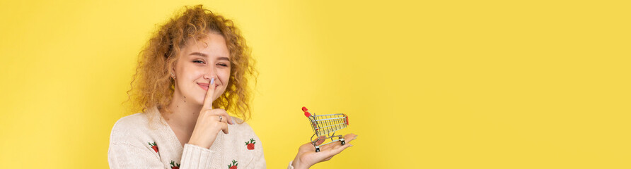Fototapeta premium A young beautiful curly red-haired girl holds a food cart in her hands. Shopping concept.