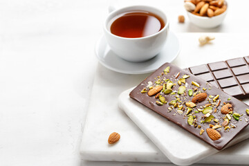 Chocolate bar with almond and pistachios on a white marble board. Two chocolate bars with tea....