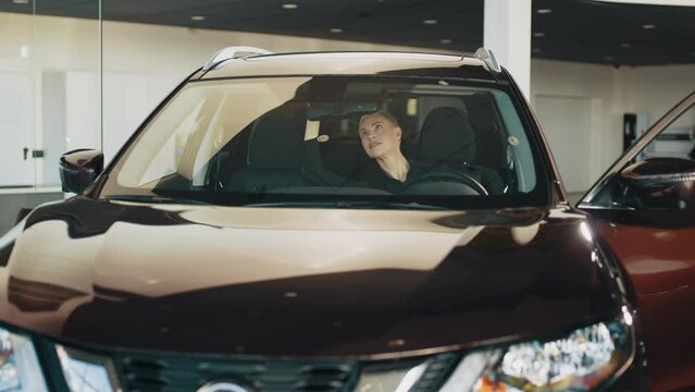 Lady in a car salon. Woman buying the car. Stylish girl sitting in the car evaluates the interior of the car inside. The woman is happy, smiling and rejoicing in the purchase new automobile.