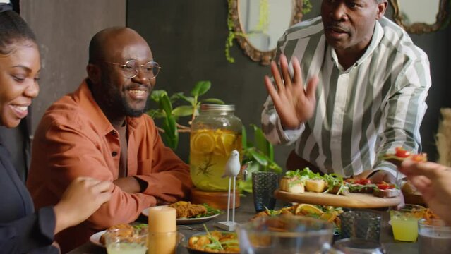 Hospitable African American man offering bruschettas to guests at family home dinner