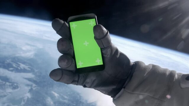 View through the helmet, astronaut using his mobile phone during the spacewalk. Green screen chroma key. Earth in the background
