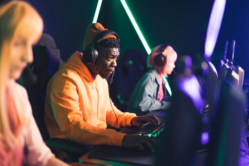 Professional cybersport gamer wearing headphones concentrating on the game with team members while...