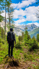 Obraz premium Man with backpack standing on rock on a hiking trail in early spring with panoramic view on the mountain peaks of Hochschwab Region in Upper Styria, Austria. Forest in Alps, Europe. Karlhochkogel