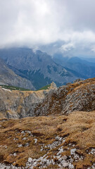 Scenic hiking trail over an alpine meadow in the cloud covered mountain peaks of the Hochschwab Region, Upper Styria, Austria. Rainy spring day in the Alps, Europe. Weather change high altitude. Wind