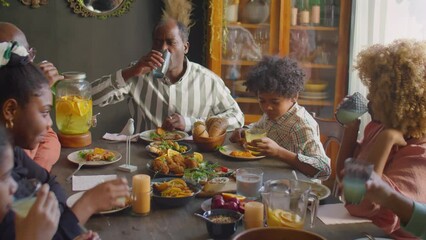 Large African American family clinking glasses in toast and drinking lemonade while having home dinner party