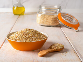 Raw white quinoa seeds in a bowl, wooden spoon and clip top glass jar on a white rustic table. Ingredient of gluten free dishes. Chenopodium quinoa for vegetarian healthy eating.