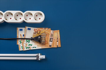 Electric plug on 50 euro banknotes, power strip and compact fluorescent light bulb over blue...