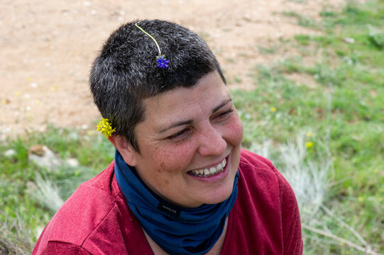 Retrato mujer con pelo corto, hablando, sentada en el suelo de la monta&ntilde;a con flores en la cabeza sonriente