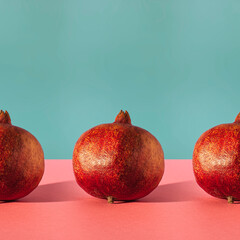 Simple square composition with row of pomegranates on two coloured background.