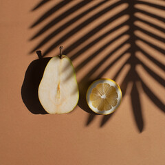 Slices of pear and lemon with palm shadow on hot summer’s day. Simple square flat lay composition on ochre background.