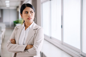 A young businesswoman stands and looks at the camera with a confident expression in the office.