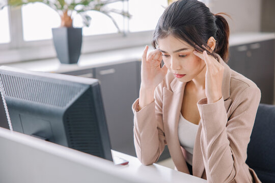 A businesswoman who works in the office looks tired and stressed by pressing her hands