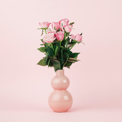 Bouquet of pink roses in peach vase on continuous pastel pink background. Simple central composition with soft light.