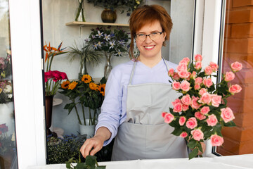 Startup, small business, flower shop. Female florist in apron holds bouquet of flowers for client, at front door of plants studio. 