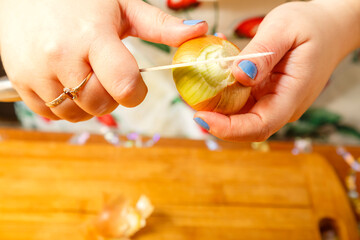 Women's hands clean the onion from the husk with a knife.